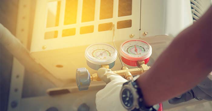 Wonder why is your HVAC not cooling? It could be because of a refrigerant leak. Pictured in the image is an HVAC tech checking the refrigerant levels of an AC unit.