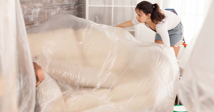 Image: a woman putting protective covers over her furniture. During a repipe, you will need to protect and cover your furniture.