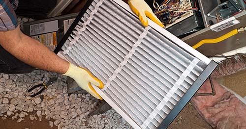 Image: a person changing out their furnace's air filter.