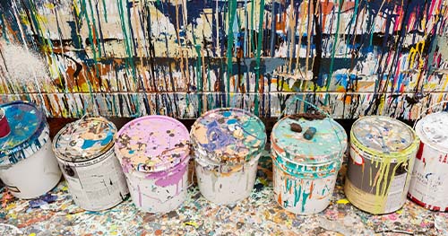Image: opened and used paint cans against a paint splattered wall.