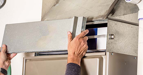 Image: a person puts the cover over the air filter box on a furnace.