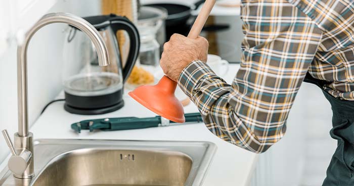 Image: a man unclogging a sink with one of the plumbing tools you should always have on hand, a cup plunger.