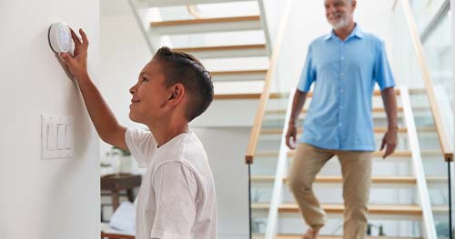 Image: a boy adjusting the thermostat when he knows he's not supposed to.