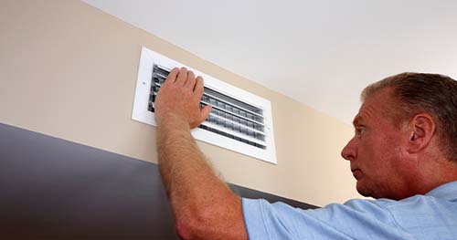 Image: a man checks his air vent to see why nothing is coming out of it.