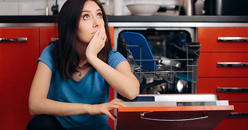 Image: a woman sits forlornly next to her broken dishwasher.