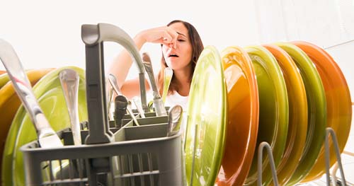 Image: a woman plugs her nose because her dishwasher smells so bad.